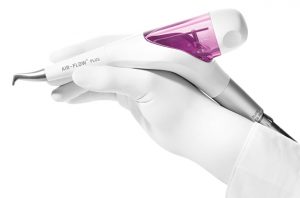 Gloved hand holding a white and purple Air-Flow dental machine